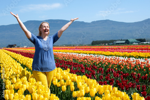 adult woman in field of tulips clothes blue yellow like flag of Ukraine joy happiness in mountains blooming Yellow flowers raise hands walk make hands heart Freedom freshness air spring