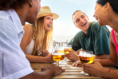 Group of multiracial young friends laughing having fun at beach bar drinking beers together. Friends on summer vacation.