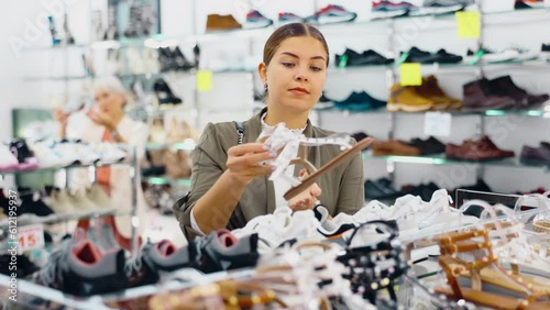 Girl client is demanding to inspect sandals in shoe showroom.Female buyer checks reliability of fastening accessories garniture on shoes