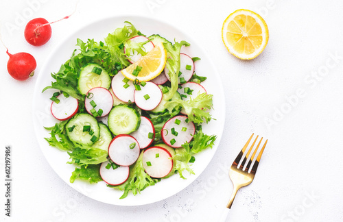 Healthy summer salad with fresh radishes, cucumbers, lettuce and green onion with greek yogurt dressing, white table background, top view