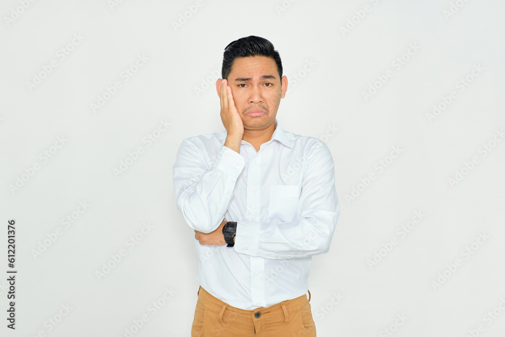 Portrait of bored young Asian man in casual clothes holding his cheek and feeling frustrated, having problems isolated on white background Portrait of bored young Asian man in casual clothes holding his cheek and feeling frustrated, having problems isolated on white background