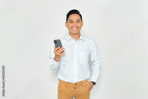 Portrait of happy young Asian man in formal wear holding smartphone and looking at camera with smile isolated on white background