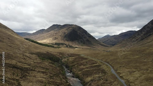 Panoramic aerial view of Scotland's rugged highlands. Remote meadow, winding road, majestic mountains, and river under a cloudy sky. Film location of Skyfall, James Bond movie. photo