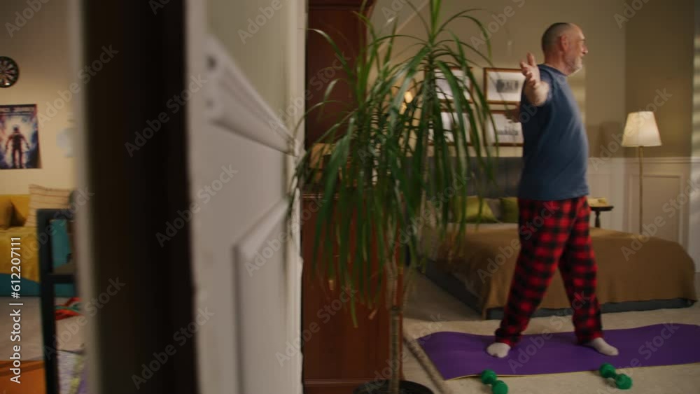 Elderly man smiles and does physical exercises in bedroom. Camera changes view to young girl stretching on training mat at home. Two apartments separated by the wall. Concept of athletic neighbours. Elderly man smiles and does physical exercises in bedroom. Camera changes view to young girl stretching on training mat at home. Two apartments separated by the wall. Concept of athletic neighbours.