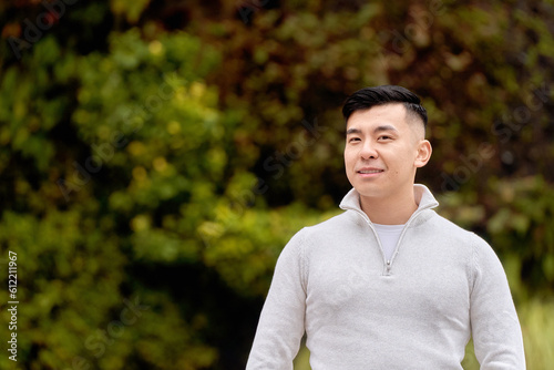 Relaxed asian man looking at the camera while standing outdoors in a park at daytime.