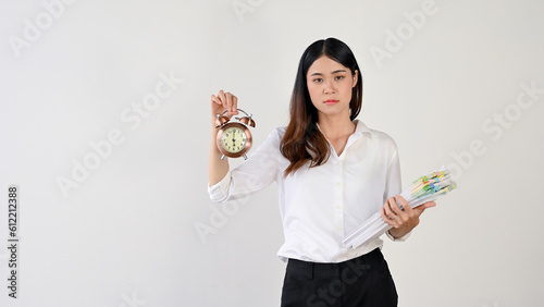A stressed and strict Asian female worker is holding an alarm clock and a pile of paperwork