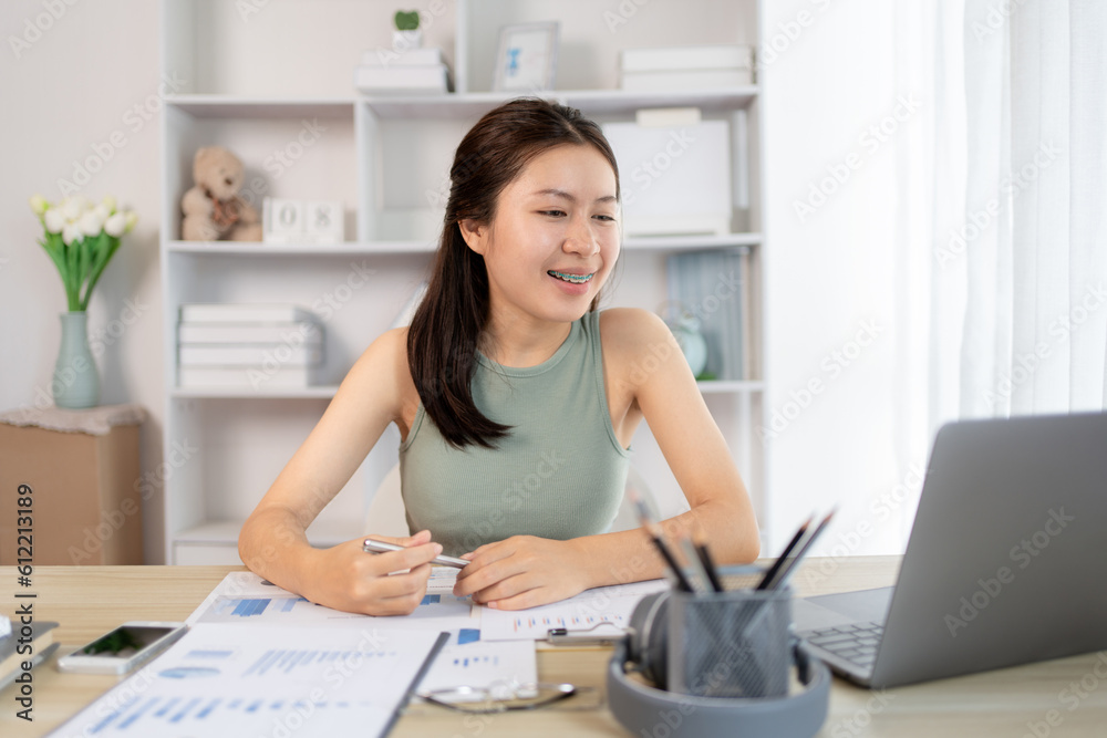 Fototapeta premium Young Asian female student watching teacher's live performance or video call on laptop in classroom at home, Conversations with teachers and classmates, Online learning, Study at your own home.