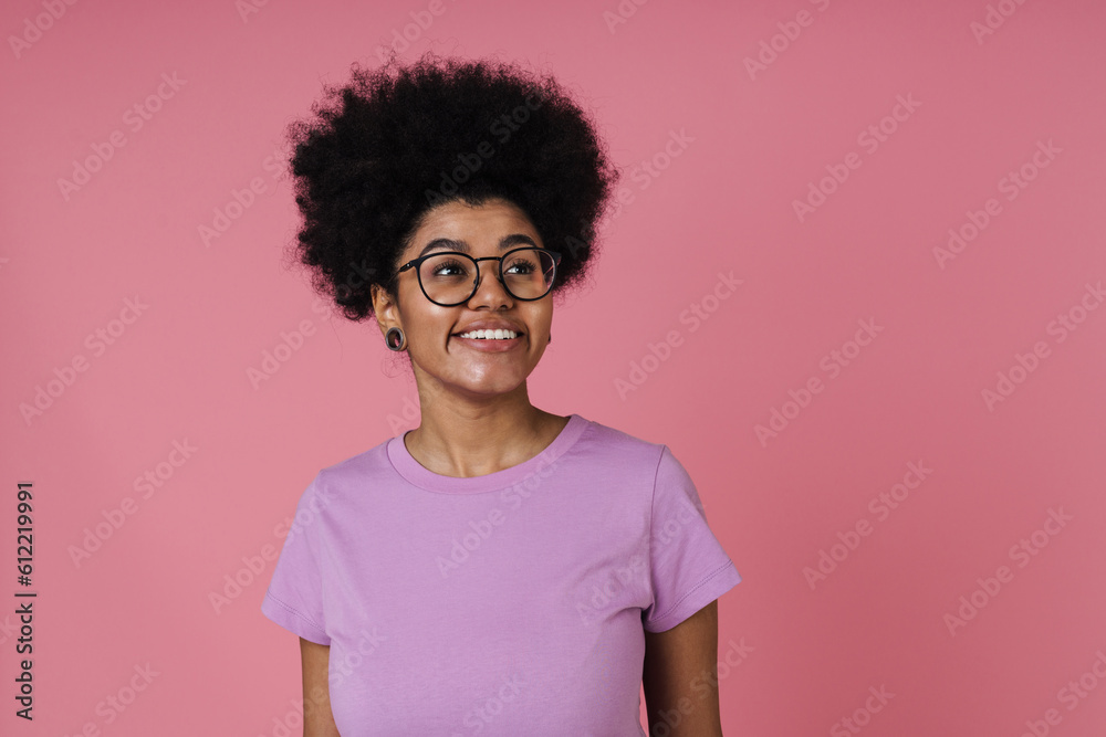 Cheerful afro woman smiling and looking away while standing isolated over pink wall
