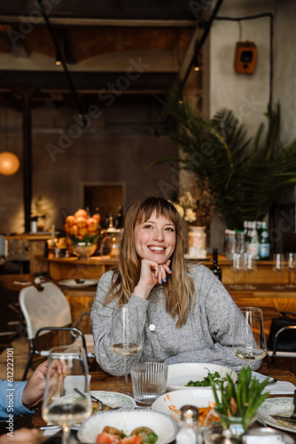 Portrait of cheerful woman drinking wine and talking with friends while sitting in restaurant