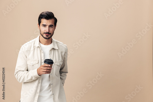 Portrait of a stylish man smile with a cup of coffee to go mock up on a beige background in a white t-shirt, fashionable clothing style, space space © SHOTPRIME STUDIO