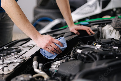 Auto mechanic working in garage man wipes the car engine. Process of repair car on service.