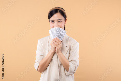 portrait of happy successful confident young asian business woman wearing white jacket holding cash money dollars standing over beige background. millionaire business, shopping concept.