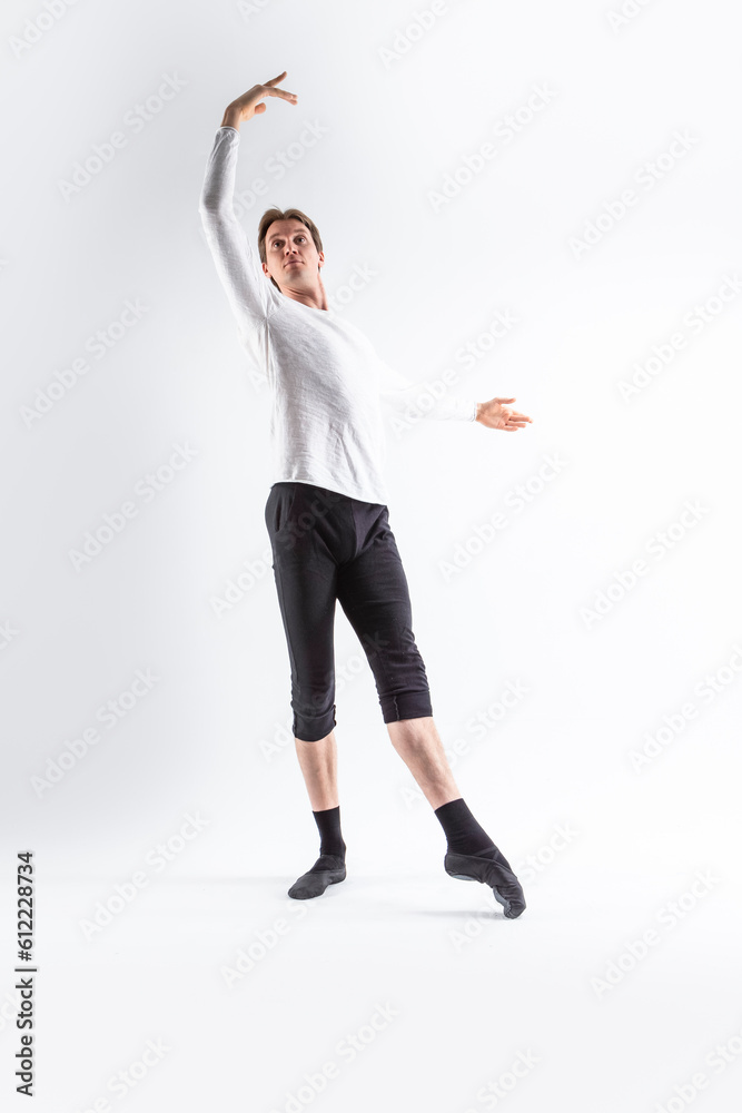 Caucasian Handsome Young Man Dancing Ballet Posing in Stretching Pose with Lifted Hands in White Shirt On White. Caucasian Handsome Young Man Dancing Ballet Posing in Stretching Pose with Lifted Hands in White Shirt On White.