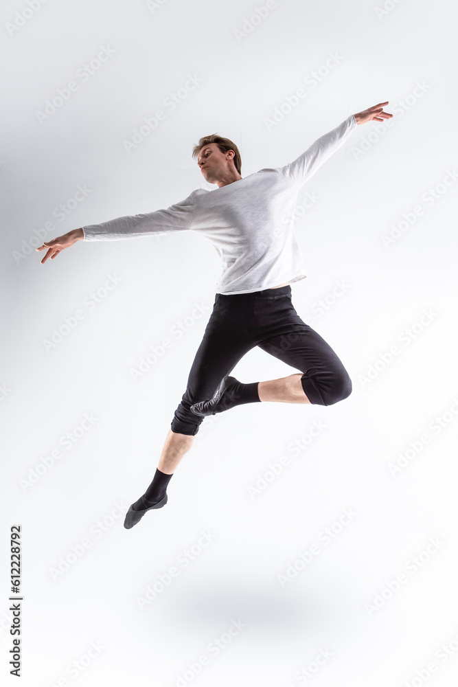 One Professional Caucasian Handsome Young Athlete Man Posing in Flying Ballet Pose with Lifted Hands in White Shirt On White.