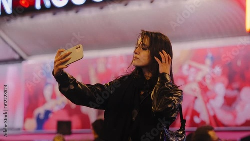 Young woman taking a selfie in front of the Moulin Rouge building, in Paris, France, at night