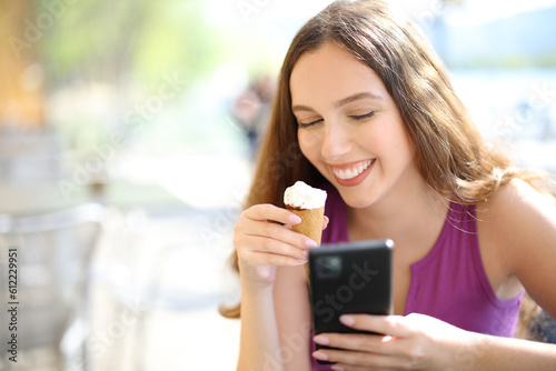 Happy woman eating ice cream and using phone in a bar