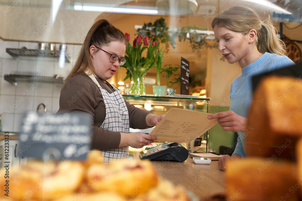 Cafe owner with down syndrome helping customer to order food from menu in coffee shop Cafe owner with down syndrome helping customer to order food from menu in coffee shop