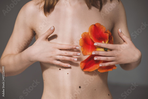 Girl in underwear with red tulip on grey background. Breast cancer awareness concept. Naked young woman covers breasts with hands. Natural beauty and acceptance of oneself in imperfect topic and scars