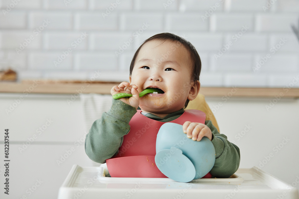 Smiling girl holding spoon in mouth sitting on high chair at home Smiling girl holding spoon in mouth sitting on high chair at home