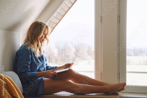 Woman using laptop sitting near attic window at home