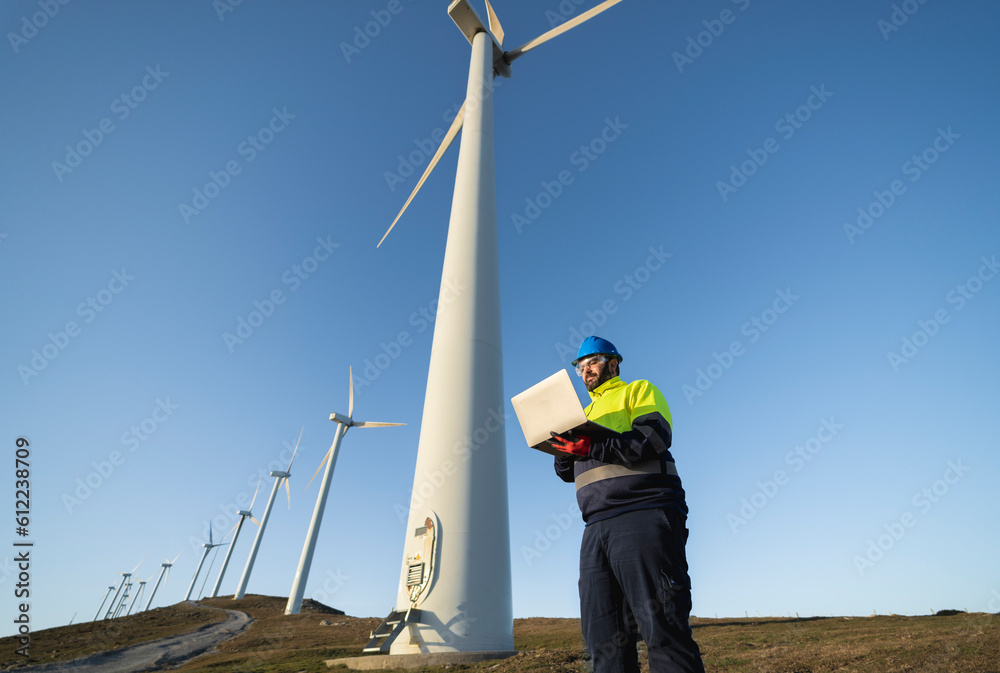 Technical engineer using laptop near tall wind turbines Technical engineer using laptop near tall wind turbines