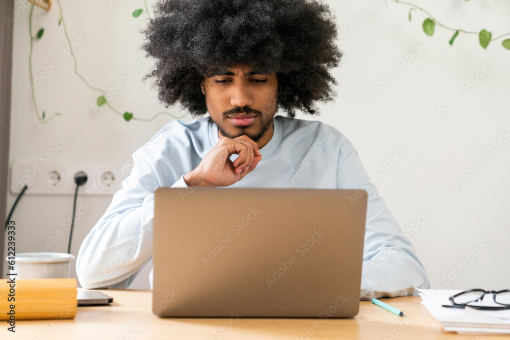 Thoughtful businessman with hand on chin working on laptop at home Thoughtful businessman with hand on chin working on laptop at home