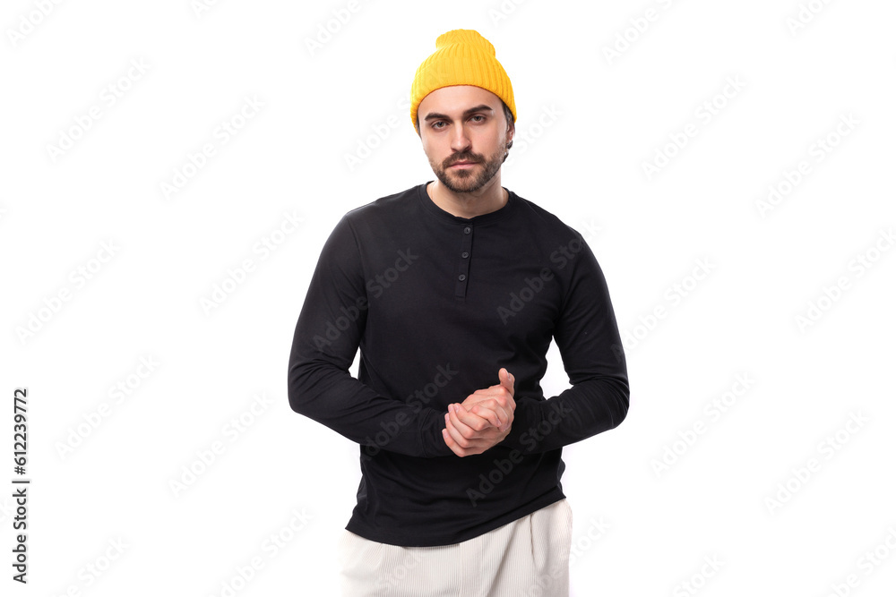 young brunette confident male model with a beard dressed in a black jacket and a yellow hat