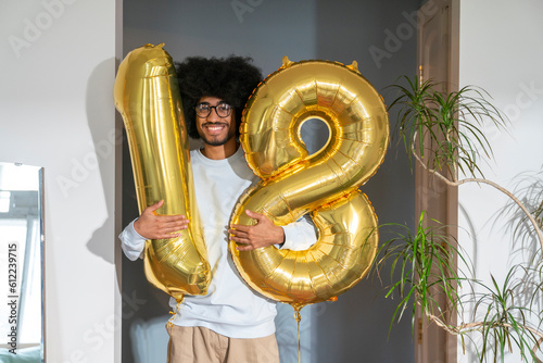Smiling man holding 18 number balloon at home photo