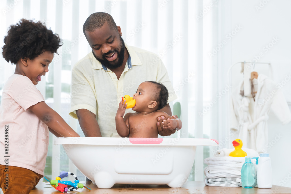 African middle aged father bathing adorable newborn baby daughter in