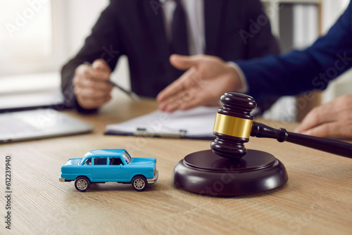 Judge gavel and miniature car symbolize auction or court case against driver who has accident and receiving vehicle insurance payment be on table in front of hands of lawyers. Selective focus