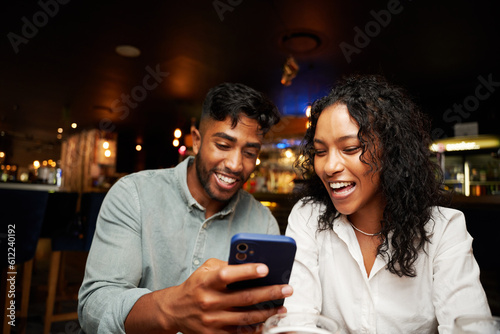 Young multiracial couple in casual clothing laughing and using smart phone at bar