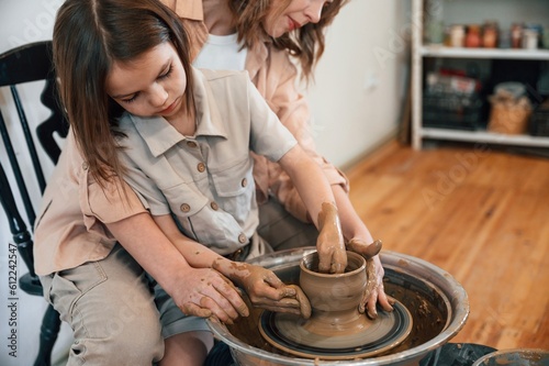Using clay to create the pot. Mother with little girl learning pottery in the workshop