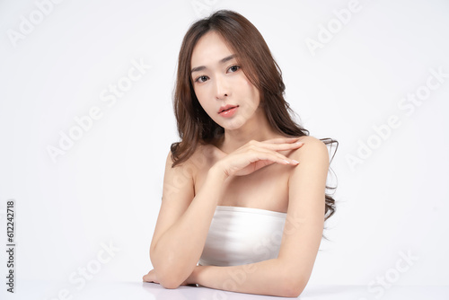 Asian woman with natural makeup smiling and touching her shoulder. Skincare and Cosmetology concept with white background. 