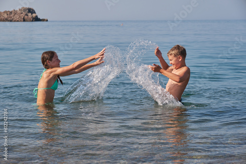 Happy joyful boy and girl swim and splash in sea. Sunny summer day, holiday vacation
