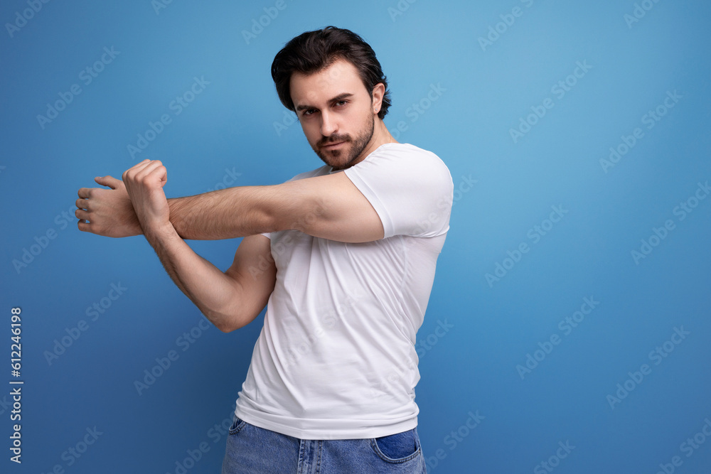 a brutal brunette guy in a white T-shirt demonstrates his strong muscles on a studio background with copy space a brutal brunette guy in a white T-shirt demonstrates his strong muscles on a studio background with copy space
