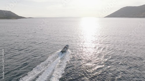 Aerial orbiting shot of motorboat speeding on Mediterranean Sea against golden sunlight at sunset in Greece, cinematic  photo