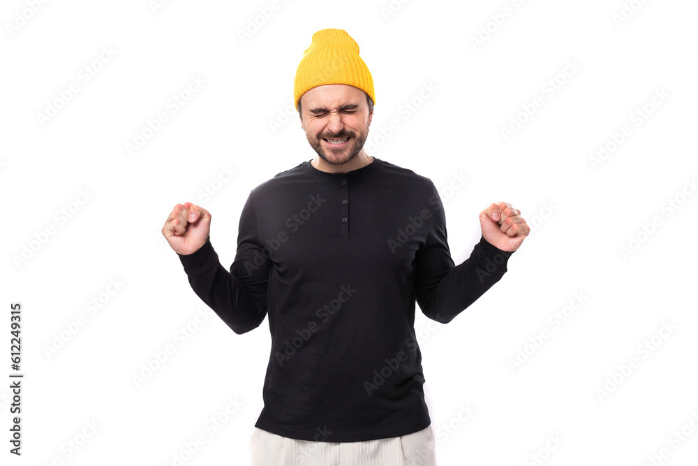 a handsome young 30 year old guy with a beard dressed in a black jacket and a yellow hat hopes with clenched fists