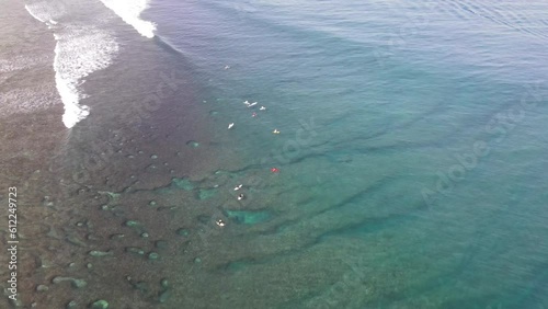 Aerial drone view of coral reef with crystal clear water and group of surfers relaxing on a surfboards waiting for waves photo