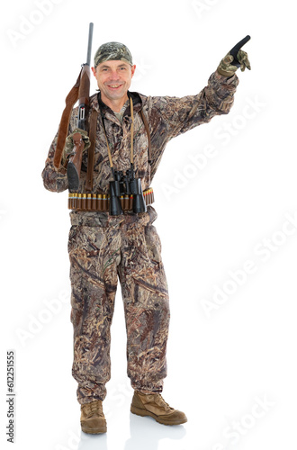 Full length portrait of happy duck hunter with a rifle and binoculars points to something to the side, isolated on white background. Fifty-year-old man in hunting uniform smiling and posing in studio.