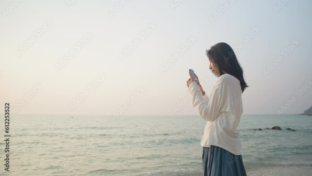 Travel. Asian woman using smartphone Take Photo on sunset at beach of Thailand Travel. Asian woman using smartphone Take Photo on sunset at beach of Thailand