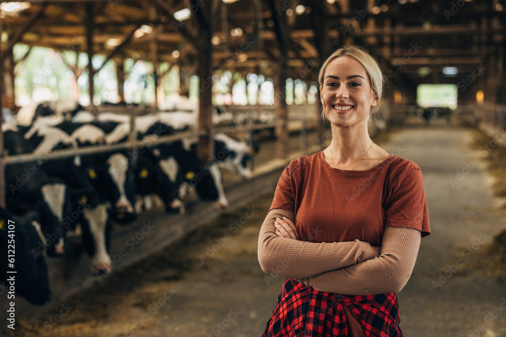 Beautiful farm girl is standing in a stable with cows.