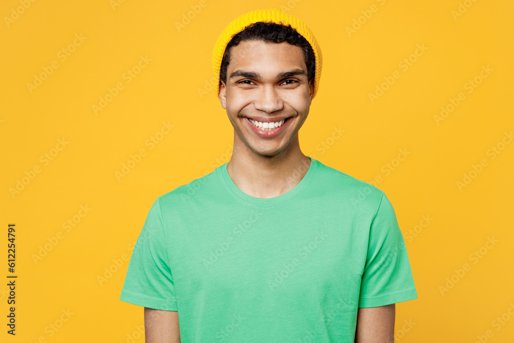 © ViDi Studio - Young smiling happy fun cool cheerful man of African American ethnicity he wears casual clothes green t-shirt hat looking camera isolated on plain yellow background studio portrait. Lifestyle concept.