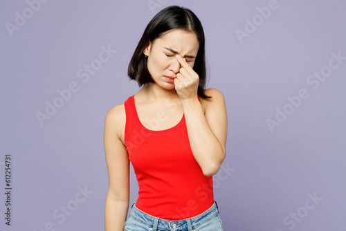Young tired woman of Asian ethnicity she wear casual clothes red tank shirt keep eyes closed rub put hand on nose isolated on plain pastel light purple background studio portrait. Lifestyle concept. © ViDi Studio