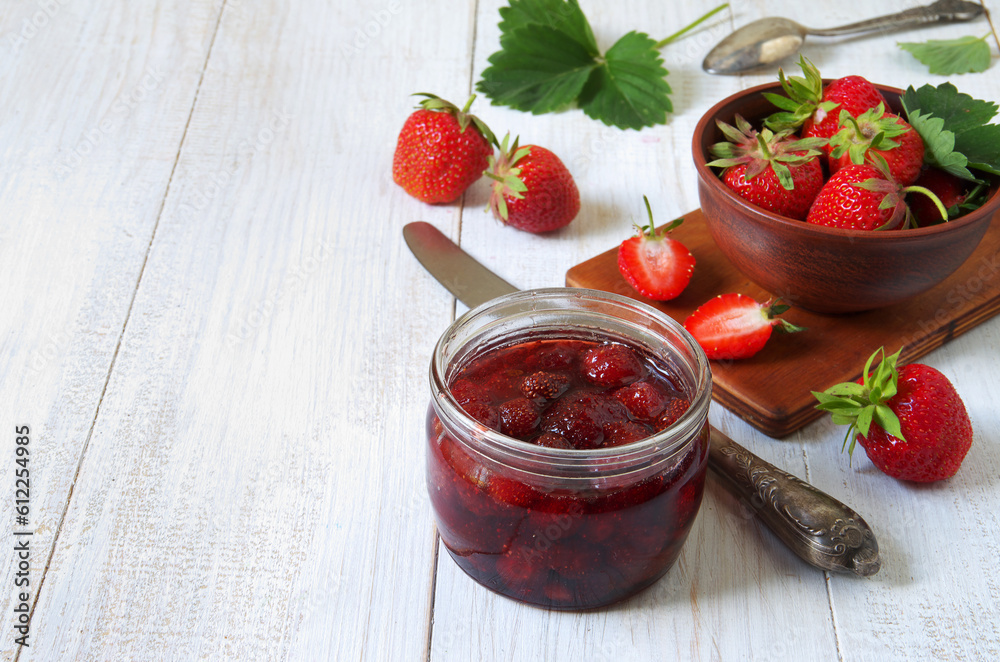 A jar of strawberry jam on a white wooden table background. A jar of strawberry jam on a white wooden table background.