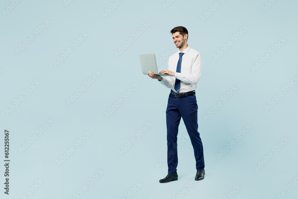 Full body young employee IT business man corporate lawyer in classic formal shirt tie work in office hold use work on laptop pc computer isolated on plain pastel light blue background studio portrait. Full body young employee IT business man corporate lawyer in classic formal shirt tie work in office hold use work on laptop pc computer isolated on plain pastel light blue background studio portrait.