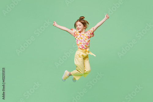 Foto Full body happy little child kid girl 6-7 years old wear casual clothes jump high raise up hands isolated on plain pastel green background studio portrait
