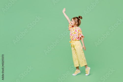 Full body side view little child kid girl 6-7 years old wear casual clothes raise up waving hand isolated on plain pastel green background studio portrait. Mother's Day love family lifestyle concept.