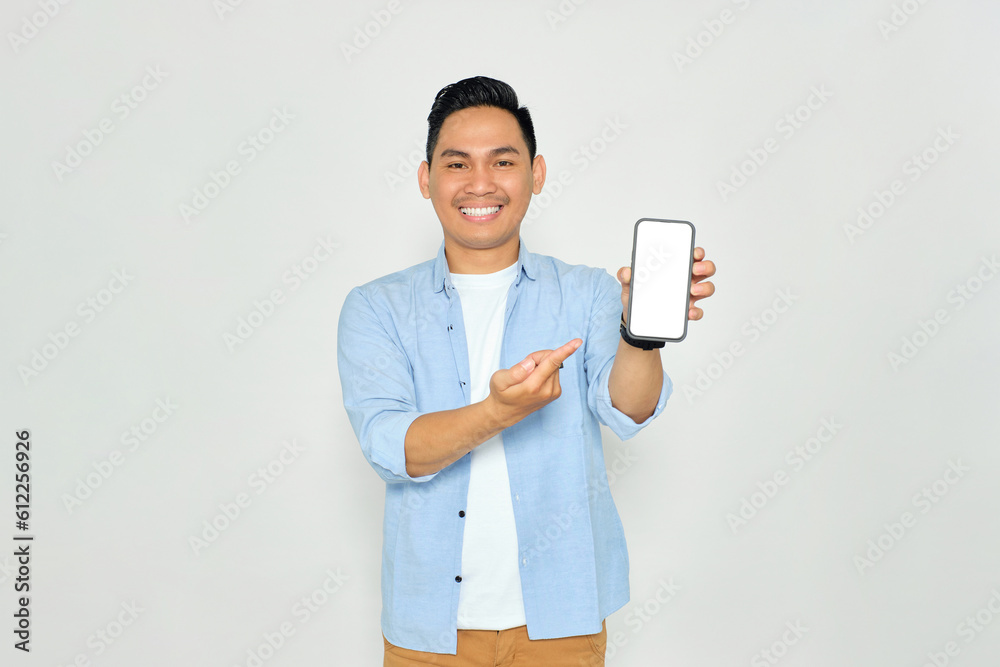 Happy young Asian man in casual clothes pointing index finger at mobile phone with blank screen isolated on white background. Advertising new mobile app, mockup concept Happy young Asian man in casual clothes pointing index finger at mobile phone with blank screen isolated on white background. Advertising new mobile app, mockup concept