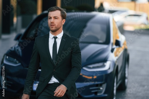 Standing, in black suit. Businessman is near his car outdoors © standret