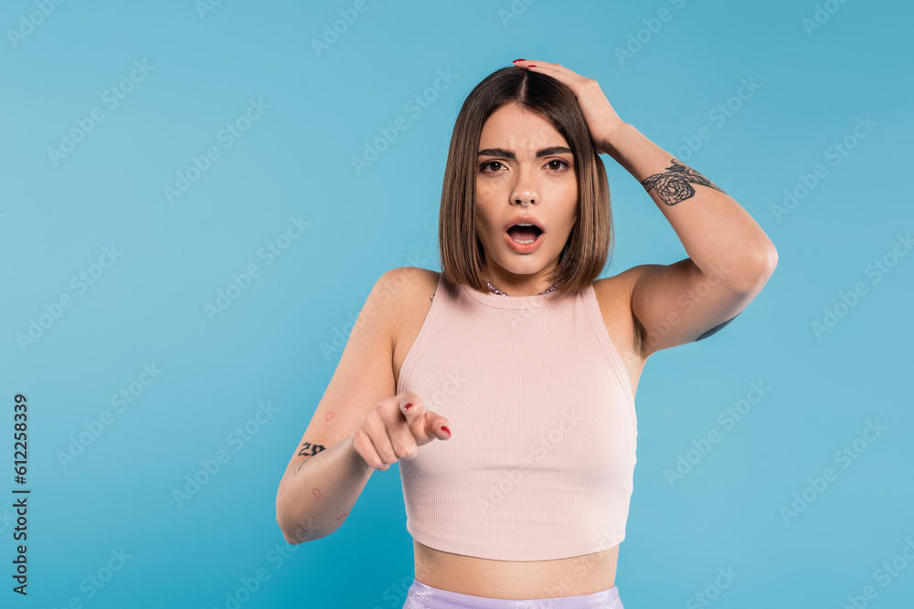 shocked face, brunette young woman with short hair, tattoos and nose piercing pointing at camera on blue background, generation z, displeased, casual attire, summer outfit shocked face, brunette young woman with short hair, tattoos and nose piercing pointing at camera on blue background, generation z, displeased, casual attire, summer outfit